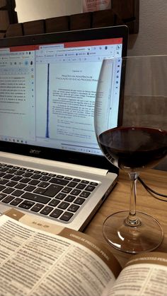 an open laptop computer sitting on top of a wooden desk next to a glass of wine