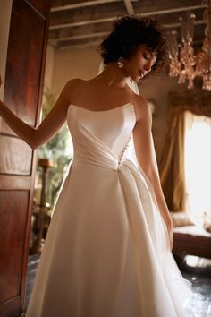 a woman in a white wedding dress is standing near a door and looking down at the floor