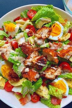 a salad with chicken, lettuce and tomatoes in it on a white plate