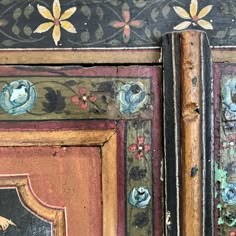 an old painted wooden door with flowers and leaves on the doors, next to another piece of furniture