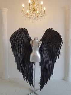 a mannequin with large black wings on it's head in front of a chandelier