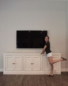 a woman leaning against a wall with her leg on the side of a white entertainment center