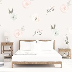 a white bed sitting next to a wall with flowers painted on it's walls