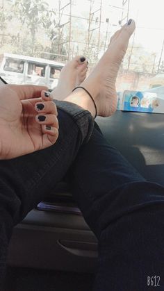 a woman's feet with black nail polish sitting in the back seat of a car