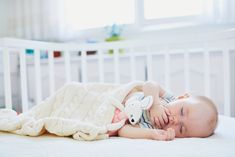 a baby laying on top of a white crib next to a stuffed animal toy