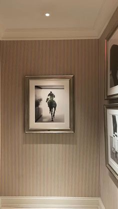 two framed photographs hang on the wall next to a toilet in a room with striped walls