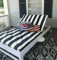 an american flag pillow on top of a white bed with black and white striped sheets