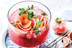 a drink with oranges and mint garnish on a plate next to other drinks