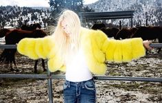 a woman standing in front of a fence with her arms out and horses behind her