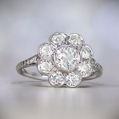 an old - fashioned diamond ring is displayed on a white surface, with the center setting surrounded by smaller round diamonds