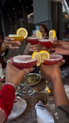 several people holding up wine glasses with lemon wedges on them while sitting at a table