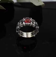 a silver ring with a red stone in the center on a black surface next to a plant