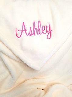 the name ashley is embroidered on top of a white blanket with pink thread in it