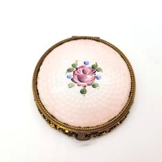 an antique pink rose brooch sitting on top of a white table next to a wall