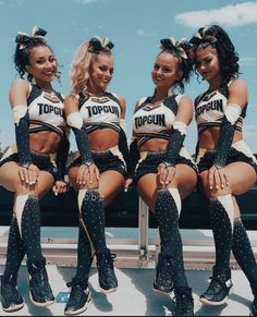 four cheerleaders are posing for a photo in their uniforms and boots, with one sitting on the bench