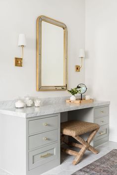 a bathroom vanity with marble counter top and gold framed mirror above it, along with two stools