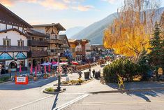 people are walking down the street in front of shops and buildings with mountains in the background