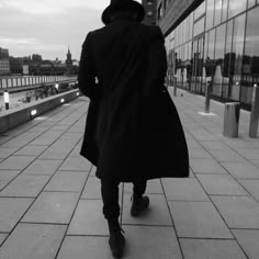 a man in a trench coat walking down a sidewalk next to a tall glass building