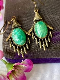 a pair of green earrings sitting on top of a purple and pink flower next to a purse