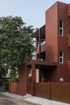 a tall red building sitting on the side of a road next to a fence and trees