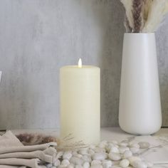 a white candle and some rocks on a table next to a vase with feathers in it