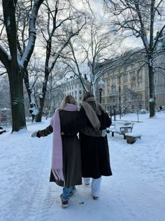 two people walking in the snow near trees