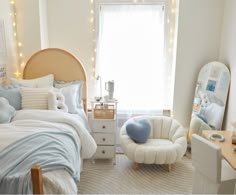 a bedroom decorated in white and blue with lights on the window sill, bed, chair, desk and mirror