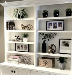 a white book shelf filled with lots of books and potted plants on top of it