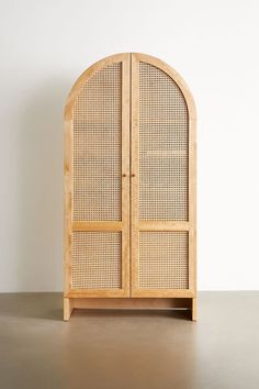 an arched wooden cabinet with wicker doors on the top and bottom, against a white wall