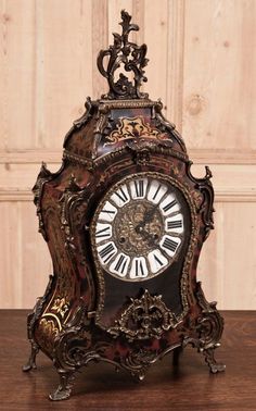 an ornate clock with roman numerals on the face and hands sits on a wooden table