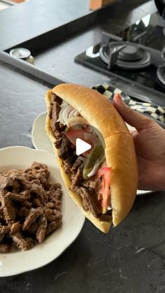 a hand holding a sandwich over a plate with some meat and vegetables on the side