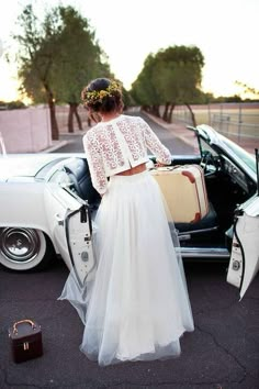 a woman in a white dress standing next to a car with her suitcase and luggage