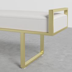 a white bench sitting on top of a cement floor next to a wall with a gold frame