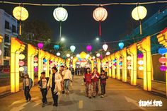 many people are walking down the street with lanterns hanging from the ceiling and lights above them