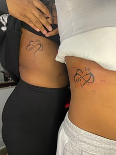 two women with tattoos on their stomachs, one has a heart and the other has an arrow