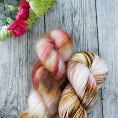 two skeins of yarn sitting on top of a wooden table next to flowers