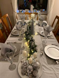 the table is set for christmas dinner with silver and white decorations on it, along with candles