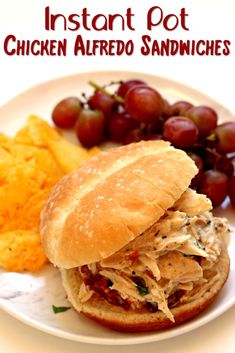 a white plate topped with a sandwich next to grapes and crackers on a table