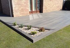 a wooden deck in front of a brick building with plants growing out of the ground