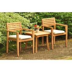 two wooden chairs sitting next to each other on a brick walkway in front of bushes