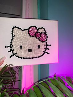 a hello kitty painting on a white canvas next to a potted plant