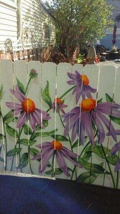 a painting of purple flowers painted on a white fence with green leaves and orange centers