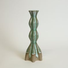 a green glass vase sitting on top of a white table next to a brown base