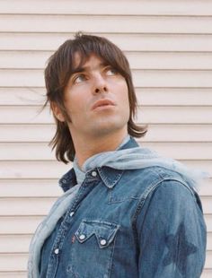 a man with long hair wearing a jean jacket looking up at something in the air