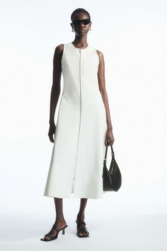 The COS womenswear team know the importance of having a staple dress or two in your wardrobe. This off-white style is crafted from a cotton blend and cut with a fitted bodice that cascades down to a subtly flared midi skirt. The modern zip gives it a laid-back ease; match your jewellery to the silver-tone hardware.  Slim fitSleeveless  65% Cotton, 28% Polyamide (Nylon), 7% Elastane / Machine wash Back length of size S is 122.2cm / Model wears a size S Cos Outfit, 2024 Clothes, Normcore Fashion, Flared Midi Skirt, Staple Dress, Midi Flare Skirt, Seersucker Dress, Woman Silhouette, Midi Shirt Dress