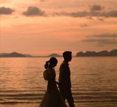 a man and woman walking on the beach at sunset