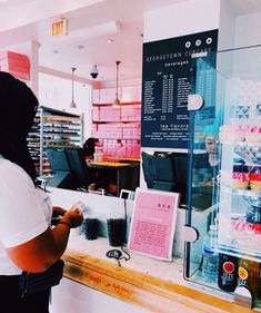 a person standing in front of a counter with donuts on it and a menu behind the counter