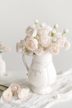 a white pitcher filled with pink roses on top of a bed next to two vases