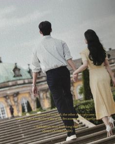 a man and woman holding hands walking down some steps in front of a large building