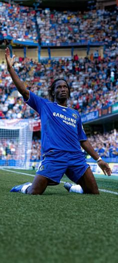 a man sitting on the ground in front of a crowd at a soccer game with his hand up